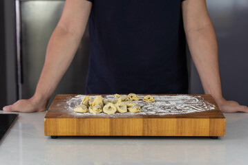 Chef cook hands making handmade Tortellini ravioli on wooden cut board with flour. Italian cuisine.