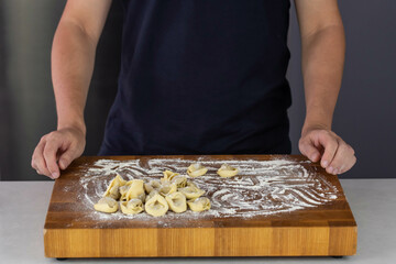 Chef cook hands making handmade Tortellini ravioli on wooden cut board with flour. Italian cuisine.