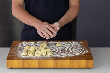 Chef cook hands making handmade Tortellini ravioli on wooden cut board with flour. Italian cuisine.