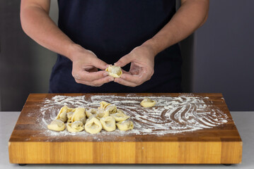 Chef cook hands making handmade Tortellini ravioli on wooden cut board with flour. Italian cuisine.