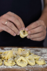 Chef cook hands making handmade Tortellini ravioli on wooden cut board with flour. Italian cuisine.
