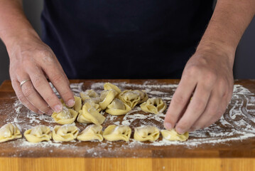Chef cook hands making handmade Tortellini ravioli on wooden cut board with flour. Italian cuisine.