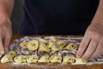 Chef cook hands making handmade Tortellini ravioli on wooden cut board with flour. Italian cuisine.