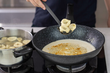 Chef cook hand making handmade tortellini ravioli with cream sauce wok pan on stove fire.