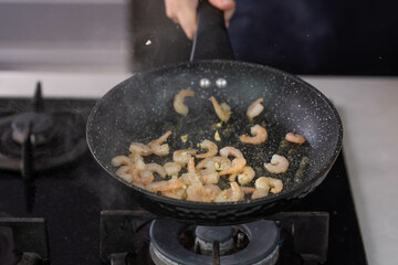Chef cook hands roasting shrimps in wok pan with oil and spice. Seafood healthy cuisine.
