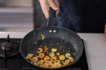 Chef cook hands roasting shrimps in wok pan with oil and spice. Seafood healthy cuisine.