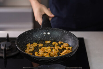 Chef cook hands roasting shrimps in wok pan with oil and spice. Seafood healthy cuisine.