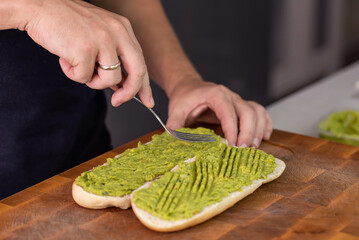 Chef cook hands making fresh diet avocado toast on bread with fork. Vegetarian and vegan cuisine. Healthy vitamin breakfast.