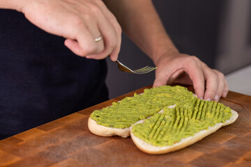 Chef cook hands making fresh diet avocado toast on bread with fork. Vegetarian and vegan cuisine. Healthy vitamin breakfast.