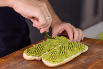 Chef cook hands making fresh diet avocado toast on bread with fork. Vegetarian and vegan cuisine. Healthy vitamin breakfast.