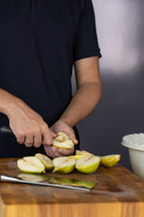 Chef cook cutting fresh pear for fruit salad on wooden cut board