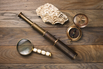 Old vintage compass, magnifying glass, ancient spyglass, shell on oak table. Travel, geography, navigation concept.