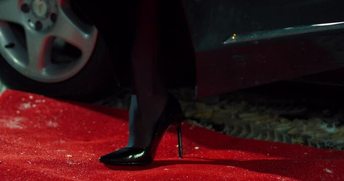 Close up of elegant woman in black high heels stepping on red carpet while going out of luxury car. Celebrity, wealth and modern lifestyles concept.