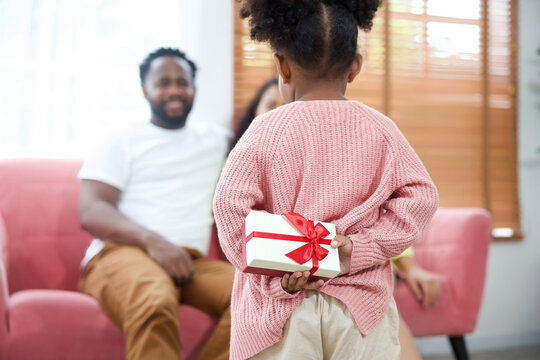 Back Girl Hiding Present Or Gift Box Giving To Mom And Dad Sitting On Sofa