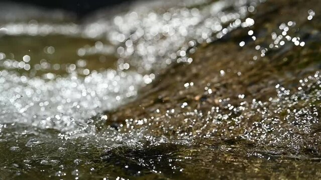 Water flows over rocks in the sunlight (slow motion, hexagonal bokeh)