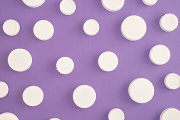 Top view of white plastic bottle caps, in a chaotic pattern on a purple background