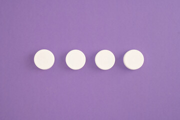 Top view of white plastic bottle caps lined up in a row on purple background