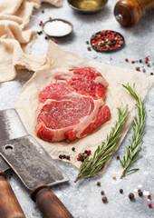 Fillet of raw beef rib eye steak on with meat cleaver,salt and pepper on light table background with tenderizer,pepper mill and kitchen towel.
