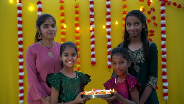 Cute Indian young and little sisters holding diya or oil lamps for Diwali Celebration.