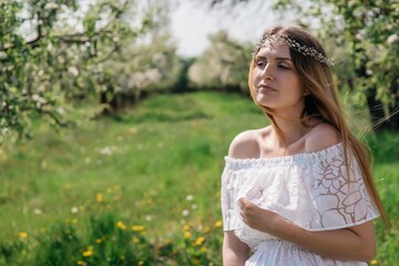 A beautiful pregnant girl in a white dress walks in an apple orchard on a sunny spring day. High quality photo