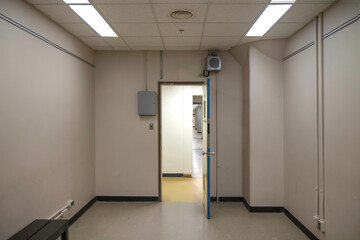 View looking out of a white room empty except for a bench, into a long empty corridor