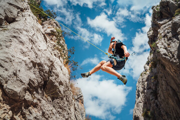 Climber teenage boy in protective helmet jumping on vertical cliff rock wall using rope Belay device, climbing harness in Paklenica canyon in Croatia. Active extreme sports time spending concept - obrazy, fototapety, plakaty