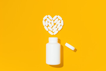 White pills in heart shape with bottle on yellow background. Mockup for advertising or other ideas....
