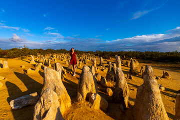 A beautiful girl in a dress walks through the pinnacles desert in western australia at sunset; unique rock formations in the desert, australian outback