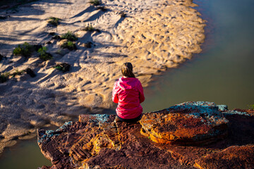 long-haired girl sits on top of a hill on the red rocks of kalbarri national park in western...