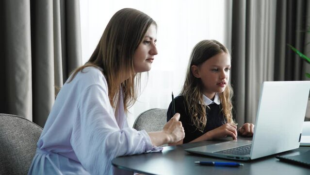 Cute small 6-7 years kid daughter learning writing with young mom tutor. Adult parent mother teaching school child girl helps with homework studying sitting at home table motivating giving five 