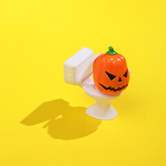 Creative layout of toilet bowl with halloween pumpkin on bright yellow background. Visual trend. Halloween concept. Minimalistic aesthetic still life with shadow. Fresh idea