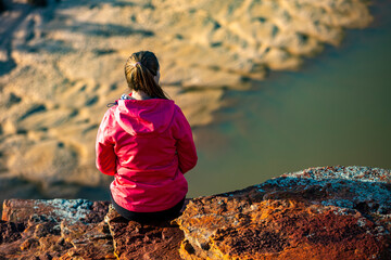 long-haired girl sits on top of a hill on the red rocks of kalbarri national park in western australia; hiking in the wilderness, australian outback