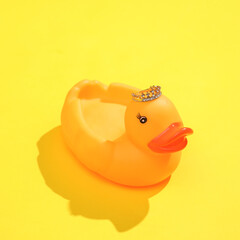 Creative layout of rubber duck with golden crown on bright yellow background. Visual summer trend. Minimalistic aesthetic still life with shadow. Fresh idea