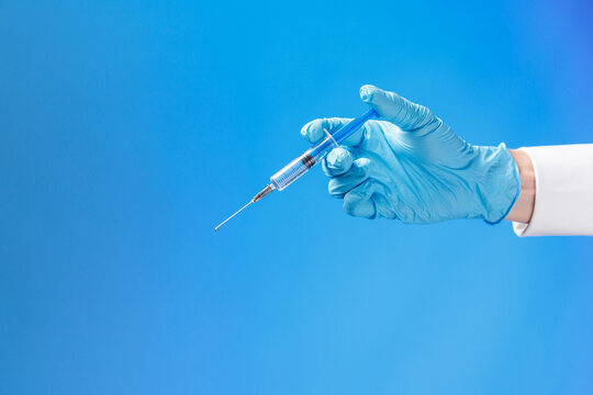 Hand In A Blue Rubber Glove Holding A Syringe Ona Blue Background.