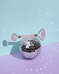 Disco mirror ball with jade facial massage roller on pastel background