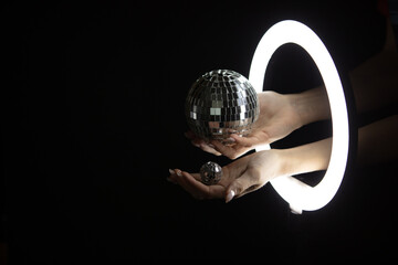 Female hands holding disco balls  through led ring lamp on black background. Party concept