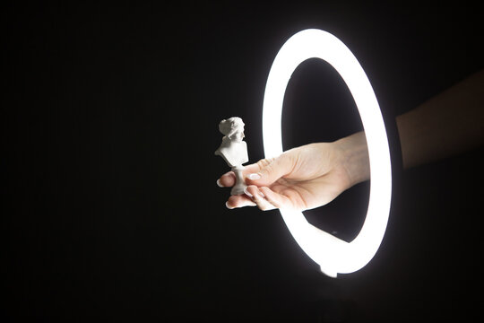 Female Hand Holding Venus Bust Through Led Ring Lamp On Black Background.