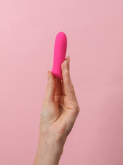 Female hand holding a clitoral vibrator on a pink background