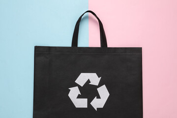Black shopping bag with circular recycling symbol on pink blue pastel background. Eco concept
