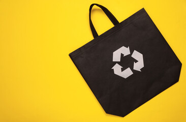 Black shopping bag with circular recycling symbol isolated on yellow background. Eco concept