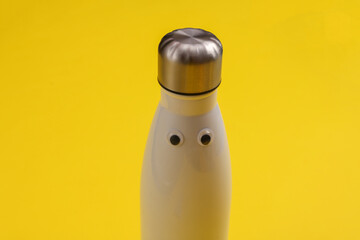 Thermos bottle with eyes on a yellow background - obrazy, fototapety, plakaty
