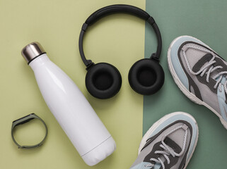 Fitness accessories on a green background. Thermos bottle, headphones, sneakers and smart bracelet. Top view