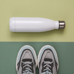 Fitness accessories on a green background. Thermos bottle and sneakers. Top view - obrazy, fototapety, plakaty