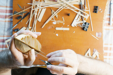 Hands of man removing excess glue from plywood details for ship model with utility knife. Process...