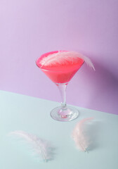 Creative layout, cocktail glass with neon slime and feathers on two tone pastel background. Visual trend. Minimalistic aesthetic still life. Party concept. Fresh idea