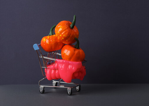 Creative Halloween Layout, Shopping Trolley With Neon Slime And Pumpkins On Two Tone Dark Background. Visual Trend. Trick Or Treat