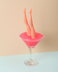 Creative layout, cocktail glass with neon slime and doll leggs on two tone pastel background....