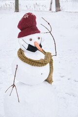 A perplexed snowman in a knitted hat and scarf with an incorrectly worn protective mask.