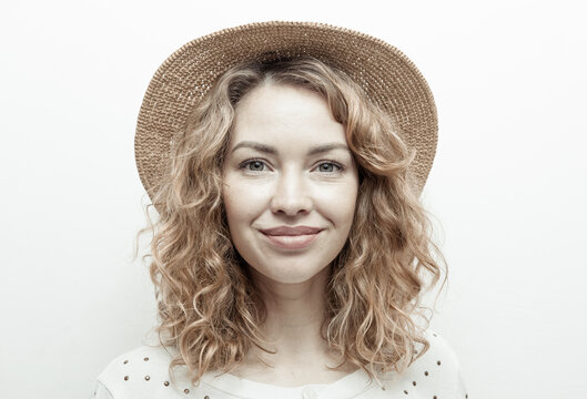 Portrait of cute smiling curly haired Caucasian woman in straw hat on white background