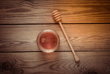 Jar of honey bee with spoon on wooden background.